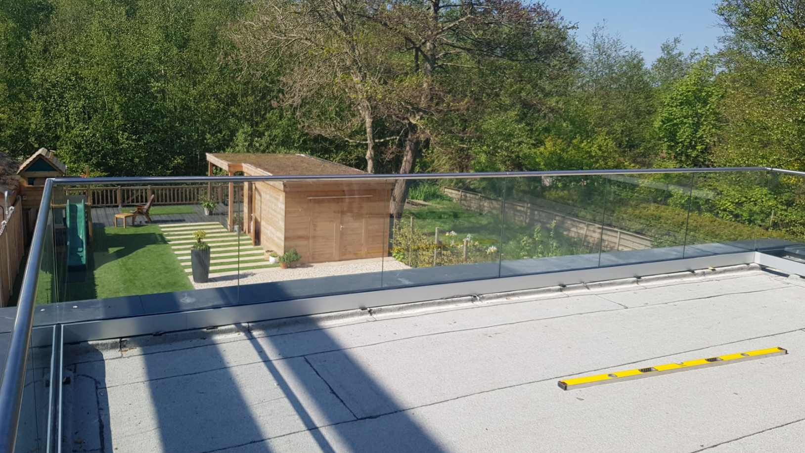 Glazen balustrade langs een dakterras met uitzicht op de tuin